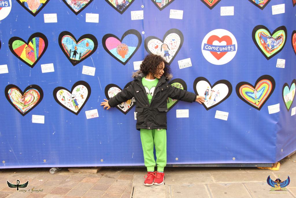 Photo of a child in green trousers in front of a wall of hearts depicting different images.
