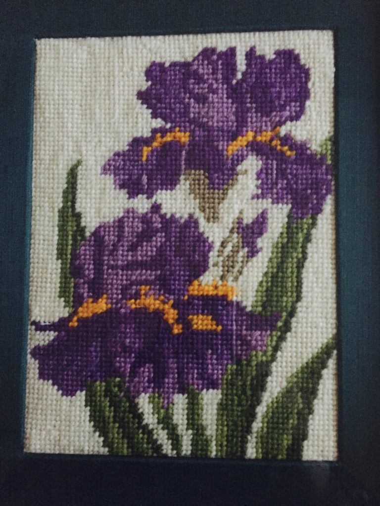 Photo showing a purple flower tapestry with green stems and yellow accents.
